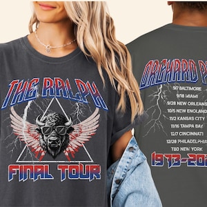 May include: Dark gray t-shirts with a vintage design. The front features a buffalo with sunglasses, wings, and the text "THE RALPH FINAL TOUR." The back displays "ORCHARD PARK" and a tour schedule from 1973-2025.