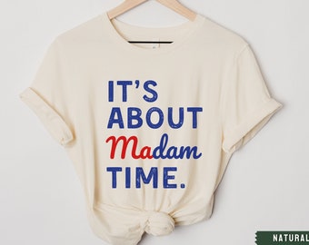 May include: A cream-colored t-shirt with the text "IT'S ABOUT Madam TIME." in blue and red lettering.