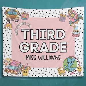 May include: A pink and white welcome banner with black polka dots. The banner says "Welcome to Third Grade Miss Williams". The banner has various illustrations including a school bus, a rocket, a globe, and books.