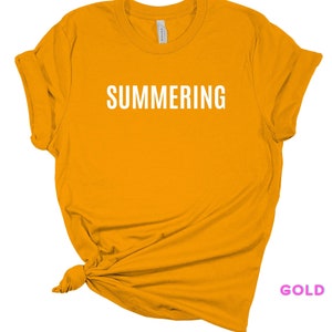May include: A gold colored t-shirt with the word "SUMMERING" printed in white on the front.