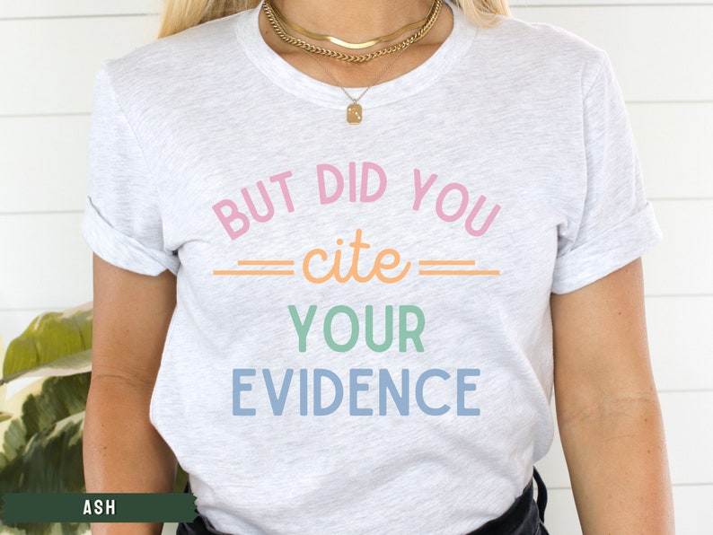 Op de afbeelding: Een wit T-shirt met de tekst "But did you cite your evidence" in regenboogkleuren.