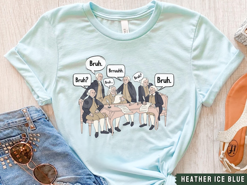 Peut inclure: T-shirt bleu clair avec un graphique des P&egrave;res fondateurs assis autour d'une table avec des bulles de dialogue qui disent "Bruh."