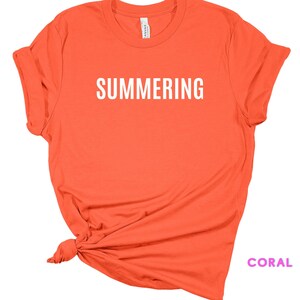 May include: Coral colored t-shirt with the word "SUMMERING" printed in white on the front.