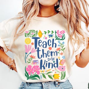 May include: A white t-shirt with a floral design and the text "Teach them to be kind".