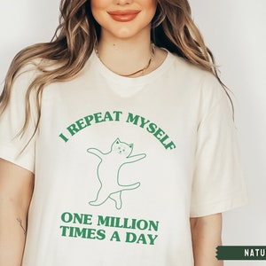 May include: A white t-shirt with a green graphic of a cat dancing and the text "I repeat myself one million times a day".
