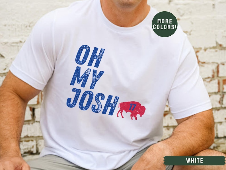 May include: White t-shirt with blue text that reads "Oh My Josh" and a red buffalo with the number 17 on it. The text has a distressed look.  The shirt is available in other colors.