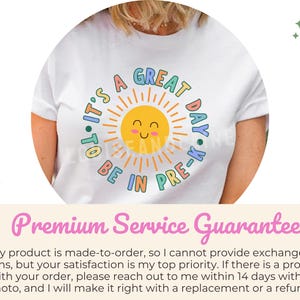 Peut inclure: Un t-shirt blanc &agrave; manches courtes avec un motif central repr&eacute;sentant un soleil jaune souriant aux rayons orange. Le texte "IT'S A GREAT DAY TO BE IN PRE-K" est imprim&eacute; dans une police multicolore circulaire autour de l'illustration.
