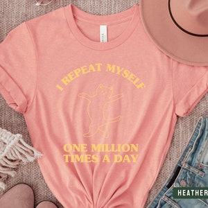 May include: A pink t-shirt with a yellow graphic of a cat and the text "I repeat myself one million times a day".