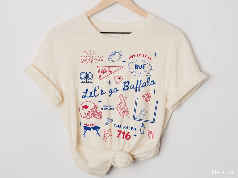 May include: Cream-colored t-shirt with a graphic design featuring the text "Let's go Buffalo" and various football-related illustrations in red and blue. Includes a football, helmet, and the number 716.