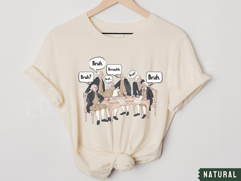 Peut inclure: Un t-shirt cr&egrave;me avec un graphique repr&eacute;sentant les P&egrave;res fondateurs assis autour d'une table avec des bulles de dialogue au-dessus de leurs t&ecirc;tes qui disent "Bruh." et "Bruh?" Le graphique est dans un style cartoon.