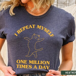 May include: A heather navy blue t-shirt with a yellow graphic of a cat and the text "I repeat myself one million times a day".