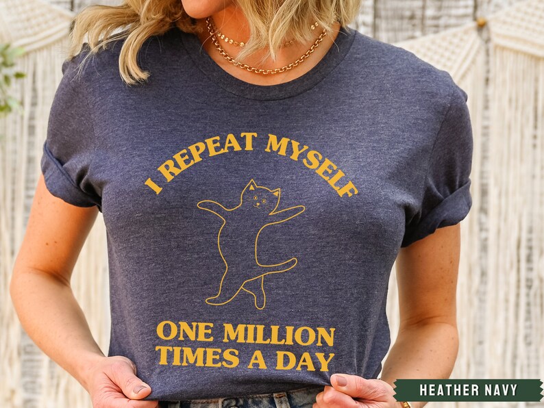 May include: A heather navy blue t-shirt with a yellow graphic of a cat and the text "I repeat myself one million times a day".