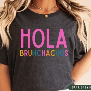 May include: Dark grey heather t-shirt with the text "HOLA BRUHCHACHOS" in pink, yellow, blue, green, and orange.