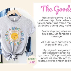 Peut inclure: Un t-shirt gris chin&eacute; &agrave; manches courtes avec un motif de soleil jaune souriant entour&eacute; de rayons. Le texte entourant le soleil indique, IT'S A GREAT DAY TO BE IN PRE-K, en lettres bleues et vertes. Le t-shirt est sur un cintre en bois.