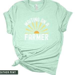 Może przedstawiać: Jasnozielony t-shirt z napisem "Waiting on a Farmer" białymi literami. Nad tekstem znajduje się ż&oacute;łte słońce z promieniami.