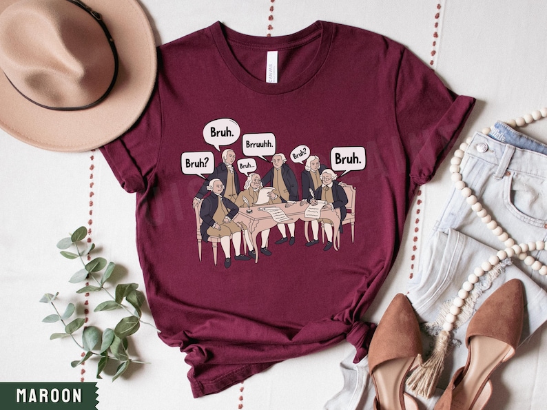 Peut inclure: Un t-shirt bordeaux avec un graphique des P&egrave;res fondateurs assis autour d'une table avec des bulles de dialogue qui disent "Bruh."