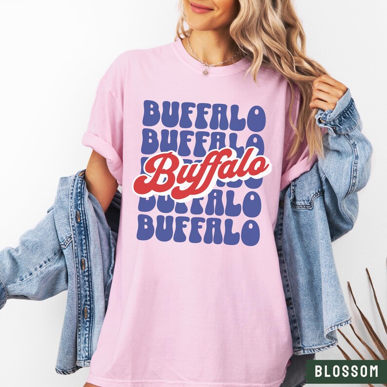 May include: A pink t-shirt with a retro-style graphic design featuring the word "Buffalo" repeated in blue and red letters.