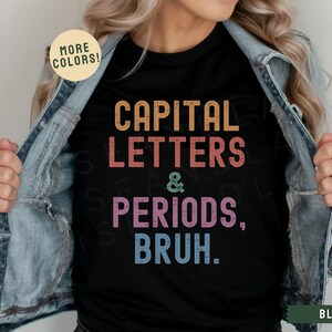 Puede incluir: Una camiseta negra con un gr&aacute;fico de estilo vintage que dice "CAPITAL LETTERS & PERIODS, BRUH." El gr&aacute;fico est&aacute; en colores arco&iacute;ris. La camiseta est&aacute; siendo modelada por una persona que lleva una chaqueta vaquera.