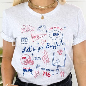 May include: Ash-colored t-shirt with a blue and red graphic design. The design includes the text "Let's go Buffalo", a football, a helmet, and the number 1. The shirt also features the text "716".