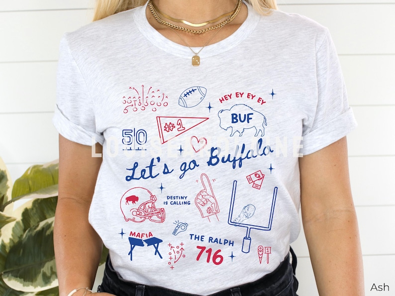 May include: Ash-colored t-shirt with a blue and red graphic design. The design includes the text "Let's go Buffalo", a football, a helmet, and the number 1. The shirt also features the text "716".