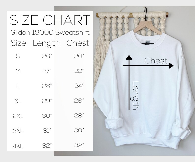 May include: A white Gildan 18000 sweatshirt hangs on a wooden hanger. A size chart shows measurements in inches for sizes S to 4XL, including length and chest dimensions. The chart is next to the sweatshirt.