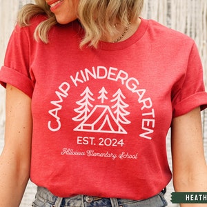 May include: Heather red t-shirt with a white graphic design that says "Camp Kindergarten Est. 2024 Hillview Elementary School" with a stylized image of a tent and pine trees.