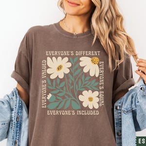 May include: A brown t-shirt with a floral design and the text "Everyone's Different, Everyone's Valued, Everyone's Equal, Everyone's Included".
