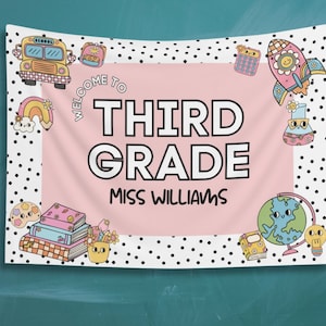 May include: A pink and white welcome banner with black polka dots. The banner says "Welcome to Third Grade Miss Williams". The banner is decorated with cartoon images of a school bus, a rocket ship, a globe, books, and a paint palette.