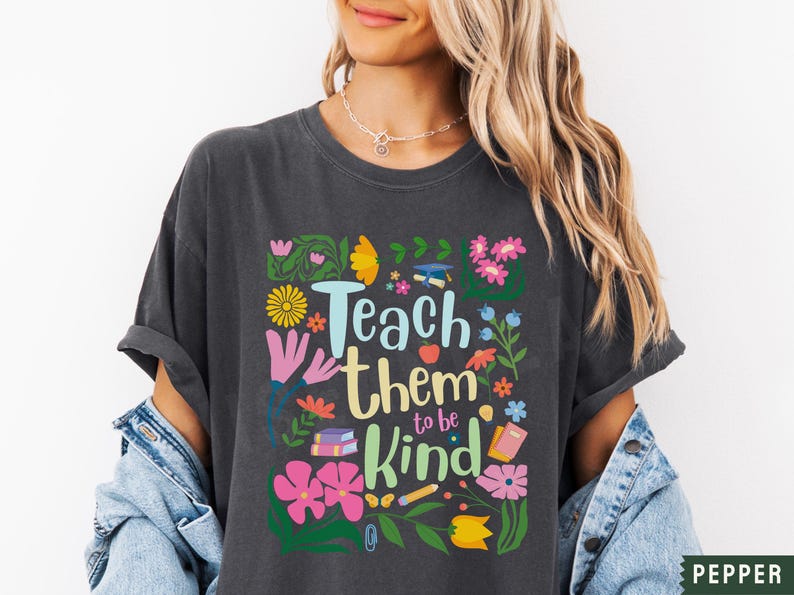 May include: A dark gray t-shirt with a colorful graphic design featuring flowers, books, pencils, and the text "Teach them to be kind".