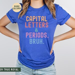 Puede incluir: Una camiseta azul real con el texto "CAPITAL LETTERS & PERIODS, BRUH." en colores arco&iacute;ris.