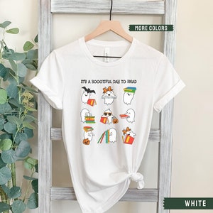 May include: White t-shirt featuring a graphic of ghosts reading books. The text on the shirt reads "It's a Boootiful Day to Read".