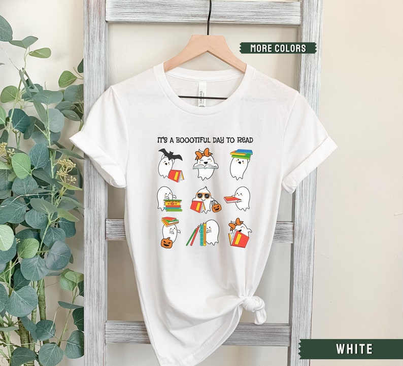 May include: White t-shirt featuring a graphic of ghosts reading books. The text on the shirt reads "It's a Boootiful Day to Read".