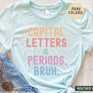 Puede incluir: Una camiseta azul claro con el texto "CAPITAL LETTERS & PERIODS, BRUH." en colores arco&iacute;ris. El texto est&aacute; en una fuente divertida y casual. La camiseta est&aacute; hecha de un material suave y c&oacute;modo y es perfecta para el uso diario.