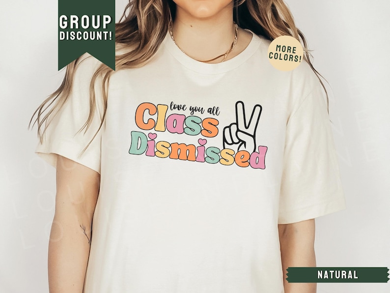 May include: A white t-shirt with the text "love you all Class Dismissed" in colorful letters with a peace sign. The shirt is on a model with long brown hair.