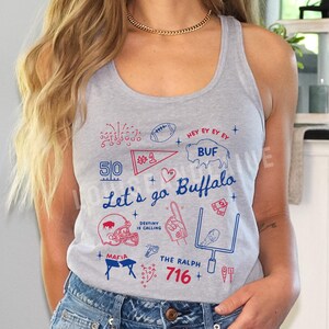 May include: Heather grey tank top with a graphic design in red and blue. The design includes the text "Let's go Buffalo", a football, a helmet, and the number 716. The tank top is sleeveless.