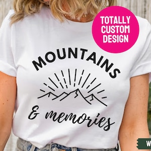 May include: White t-shirt with black text that reads "MOUNTAINS & memories" with a graphic of mountains and a sun. The text "TOTALLY CUSTOM DESIGN" is in a pink circle on the top right corner of the shirt. The word "WHITE" is in a white rectangle with a black border on the bottom right corner of the image.