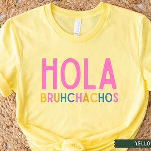 May include: Yellow t-shirt with the text "HOLA BRUHCHACHOS" in pink, orange, yellow, green, and blue letters.