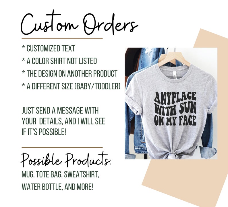 May include: A gray t-shirt with the text "ANYPLACE WITH SUN ON MY FACE" in black. The text is in a retro font style. The t-shirt is on a hanger and is displayed against a denim jacket background.