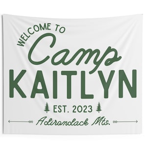 May include: White canvas wall tapestry with green text that reads "Welcome to Camp Kaitlyn Est. 2023 Adirondack Mts." The tapestry is 60 inches by 50 inches.
