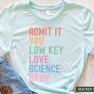 May include: A light blue t-shirt with the text "ADMIT IT YOU LOW KEY LOVE SCIENCE, BRUH" in rainbow colors.