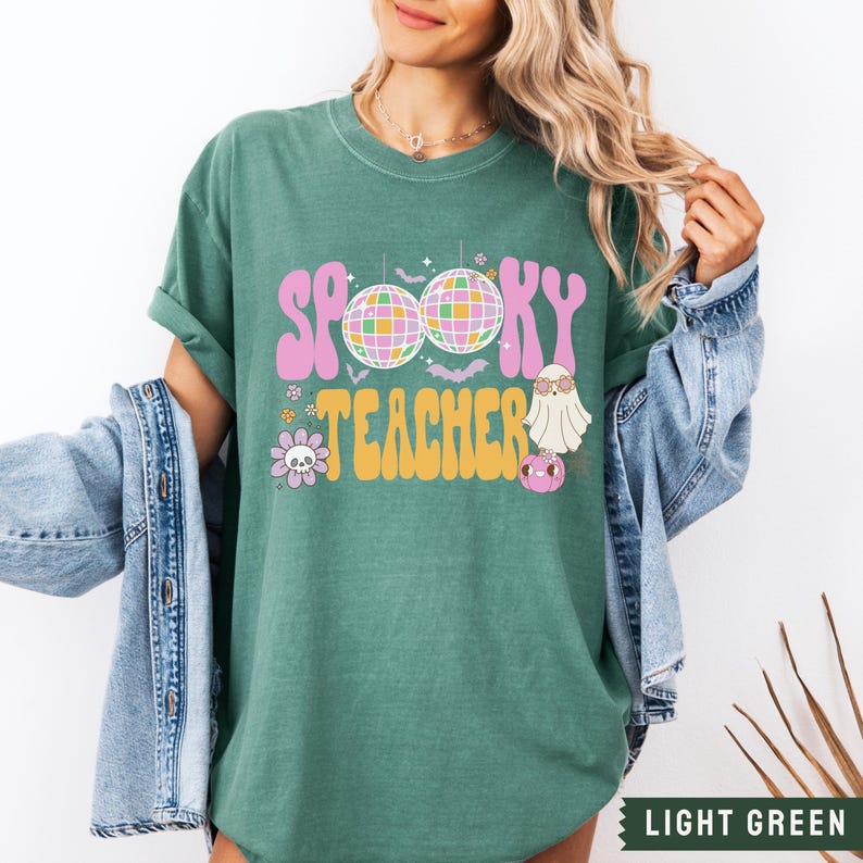 Peut inclure: Un t-shirt vert clair avec le texte "Spooky Teacher" dans une police r&eacute;tro. Le design comprend des boules disco, des chauves-souris et un fant&ocirc;me portant des lunettes de soleil.