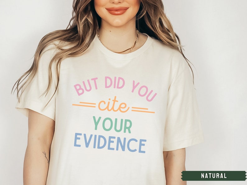 Op de afbeelding: Een wit T-shirt met de tekst "But did you cite your evidence" in regenboogkleuren. De tekst is in een speels lettertype.
