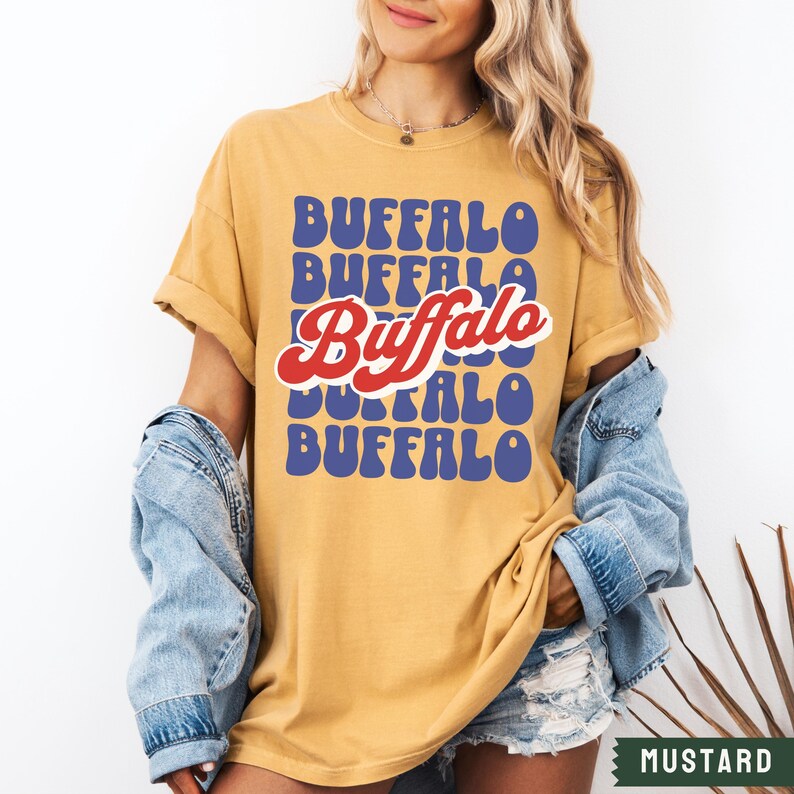 May include: A mustard yellow t-shirt with a retro-style graphic that says "Buffalo" in blue and red letters.
