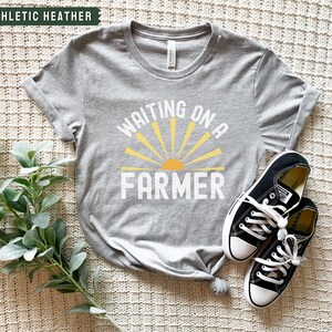 Może przedstawiać: Szary T-shirt z napisem "Waiting on a Farmer" w kolorze białym i ż&oacute;łtym graficznym słońcem.