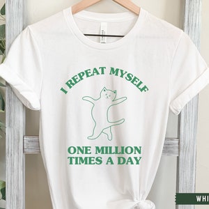 May include: White t-shirt with green text that reads "I repeat myself one million times a day". A green line drawing of a cat is above the text.