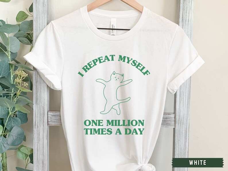 May include: White t-shirt with green text that reads "I repeat myself one million times a day". A green line drawing of a cat is above the text.