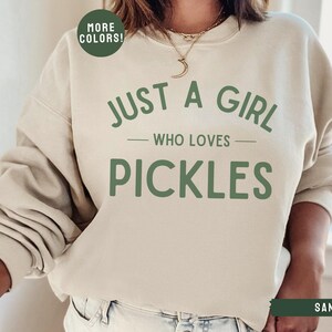 May include: A beige sweatshirt with the text "Just a girl who loves pickles" in green lettering.