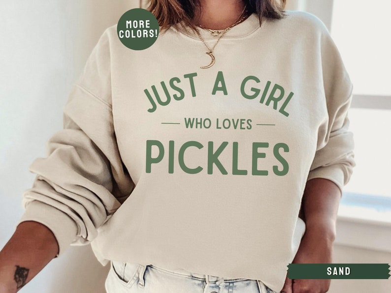 May include: A beige sweatshirt with the text "Just a girl who loves pickles" in green lettering.