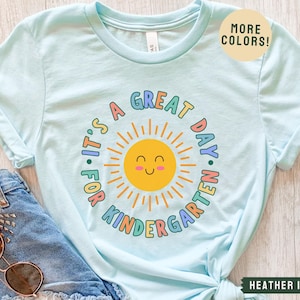 May include: A light blue t-shirt with a rainbow design that says "It's a Great Day for Kindergarten" with a smiling sun graphic.
