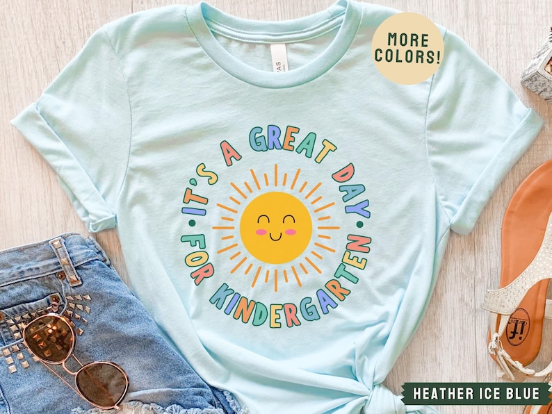 May include: A light blue t-shirt with a rainbow design that says "It's a Great Day for Kindergarten" with a smiling sun graphic.